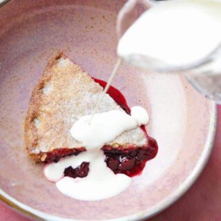 blackcurrant plate pie slice in bowl jug of cream pouring.